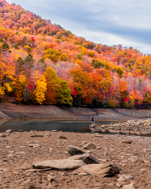Man standing on the shore of lake fontana in front of the autumn leaves in the smoky mountains