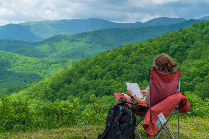 Woman sitting on a folding chair reading on a scenic mountain vista