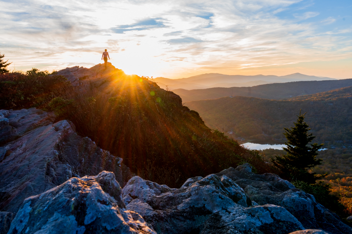 Man walking up mountain peak as the sun sets behind him