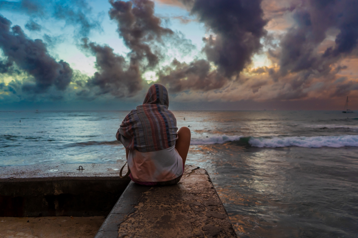 Woman sitting on the edge of a pier as the last sunlight falls behind the cloudy horizon