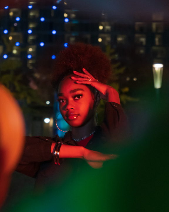 Woman holding her hands on a frame around her face with various colors being shown at her at night
