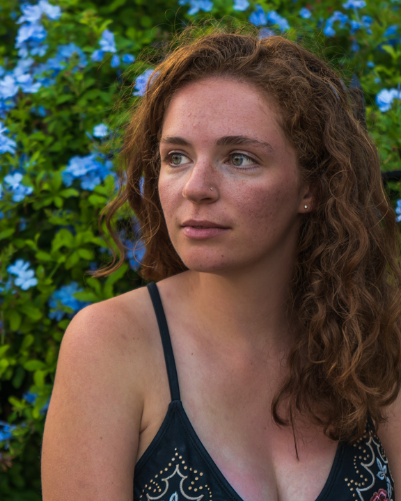 woman gazing off into the distance in front of a bush of blue flowers