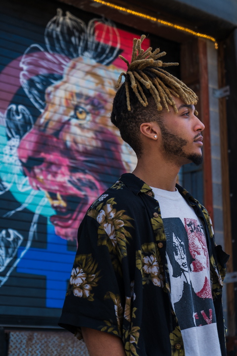 Man facing to the right with a background mural of a lion facing to the left back to back with the man