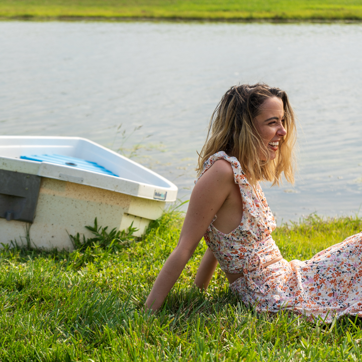 Woman in a floral dress sitting lakeside by a boat